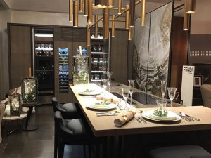 interno showroom a Londra in primo piano l'isola della cucina con snack rivestito in pelle galuchat, l'isola è un monoblocco di marmo. Sullo sfondo le colonne cucina con cantine per vino sulla destra il quadro dell'artista Giovanni Bressana